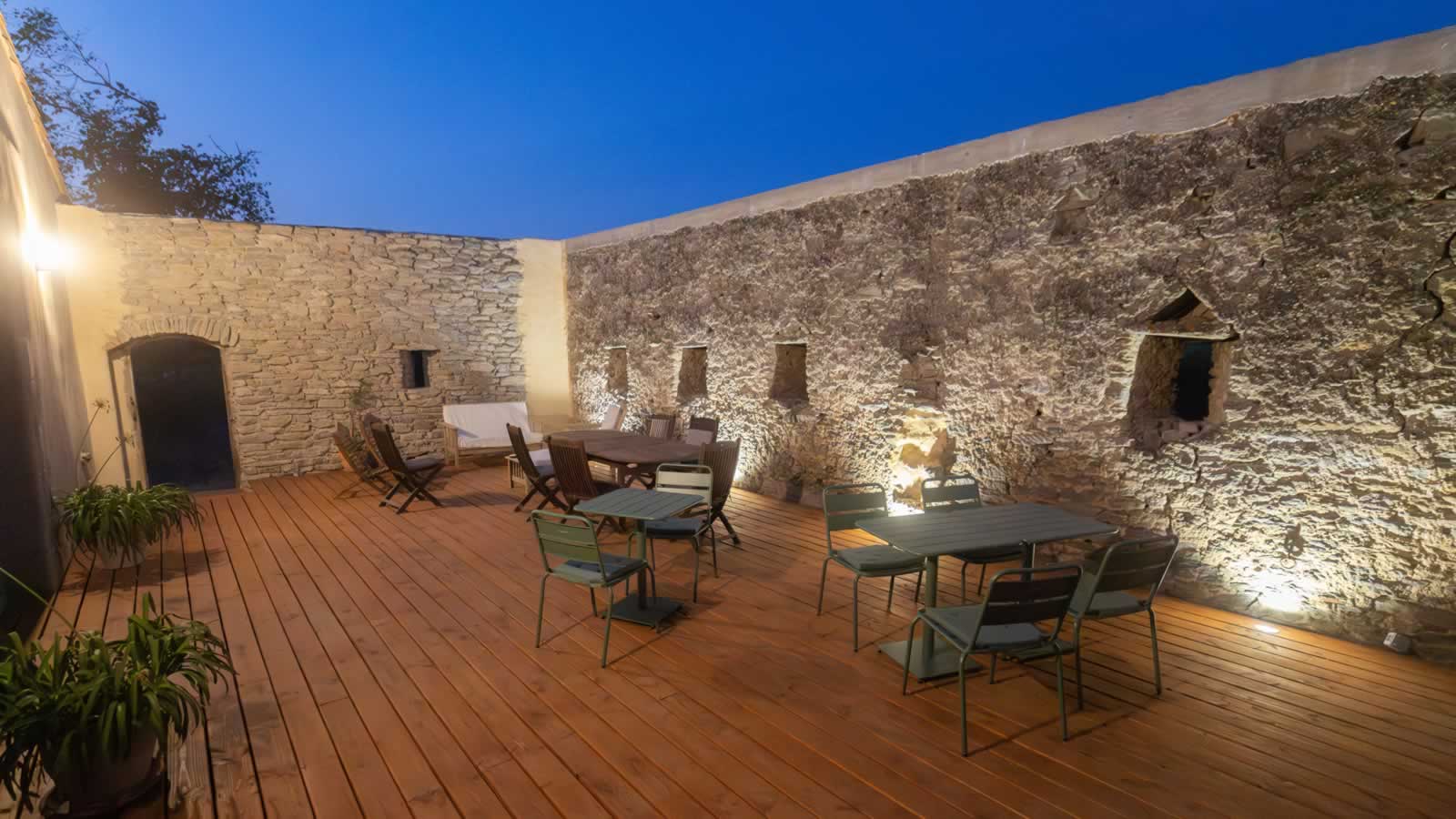 Charming outdoor patio at night with wooden deck, stone walls, and dining areas at Domaine des Périès Boutique Farmhouse, South of France